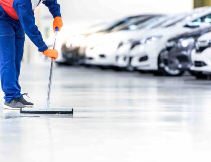 Rengøringsassistent vasker gulv hos en bilforhandler. Rengøringskoncept for butikker.